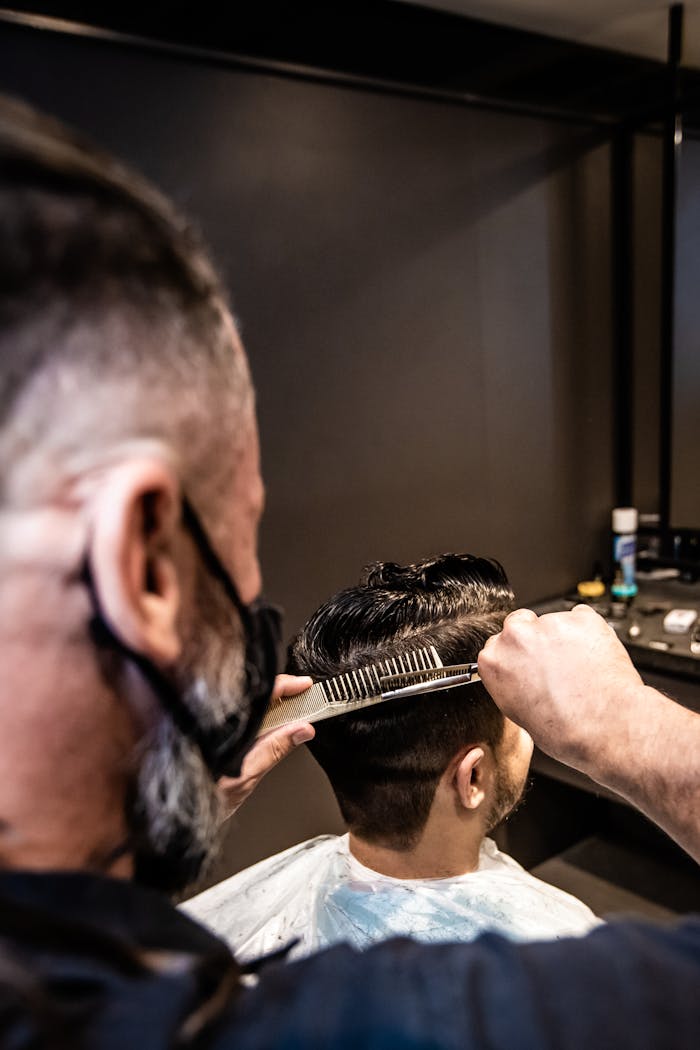Barber using scissors and comb to style male client's hair in modern salon.